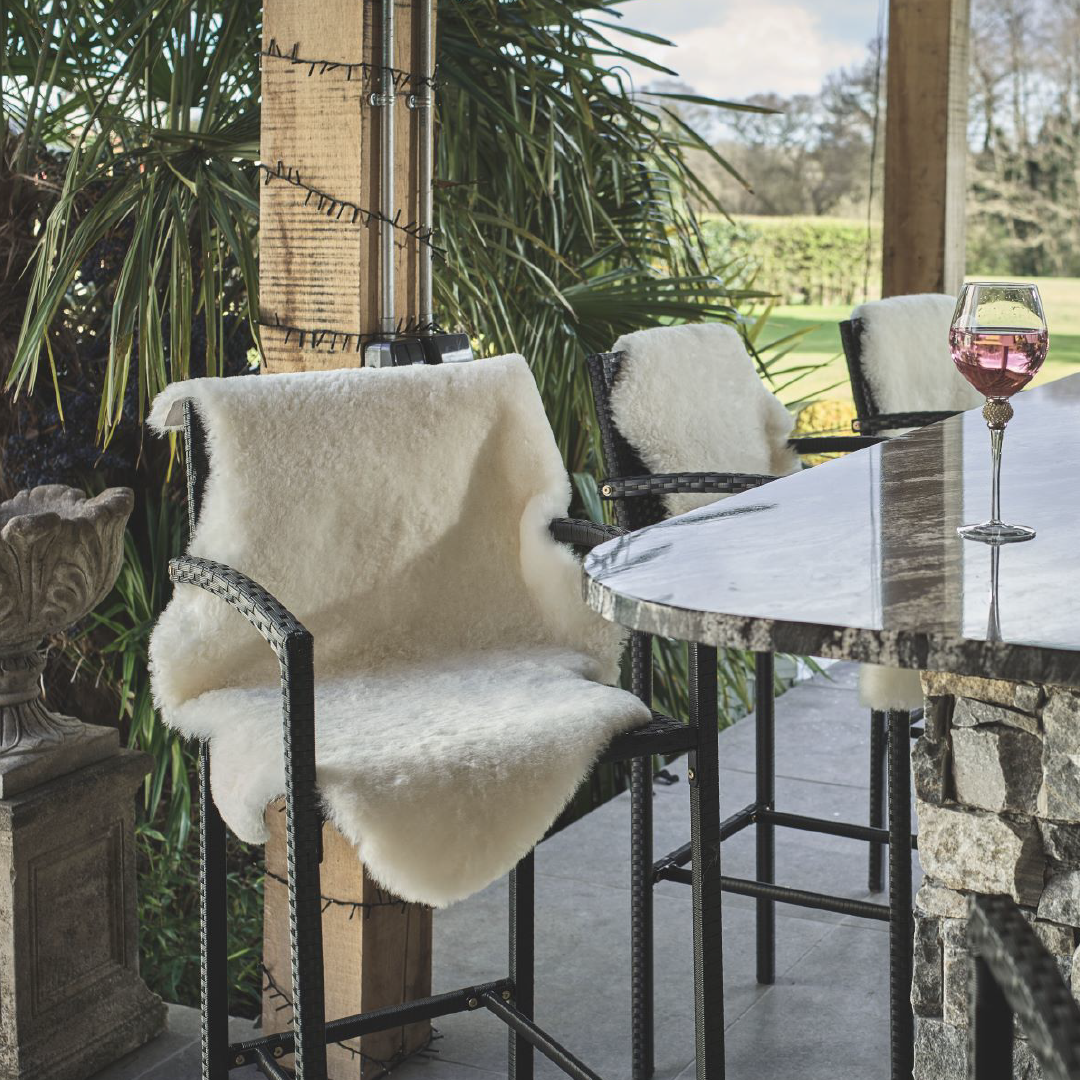 An ivory shortwool sheepskin draped over a stool at an outdoor bar area.