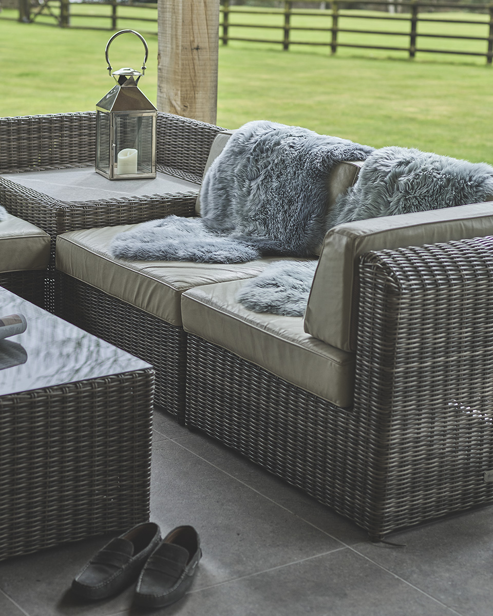 Grey sheepskins over rattan outdoor furniture sofa in a garden.