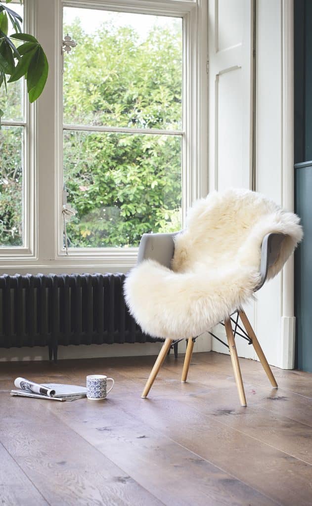 sheepskin rug used as a throw over a chair with wooden legs, infront of a large window