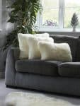 Grey sofa with soft ivory faux fur cushions in a modern living room, styled with a tall green plant and natural light from a window.