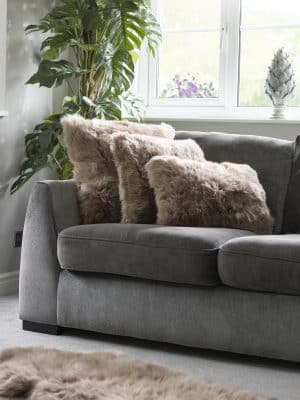 Grey sofa with soft taupe faux fur cushions in a modern living room, styled with a green plant and natural light from a window.
